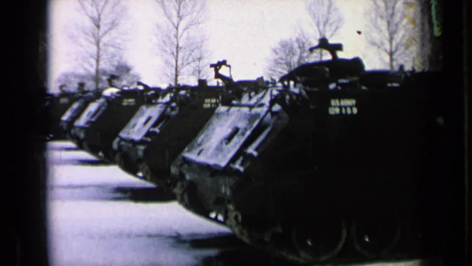 A row of U.S. Army armored vehicles appears aligned on a paved Germany base area in this 1963 8mm frame.