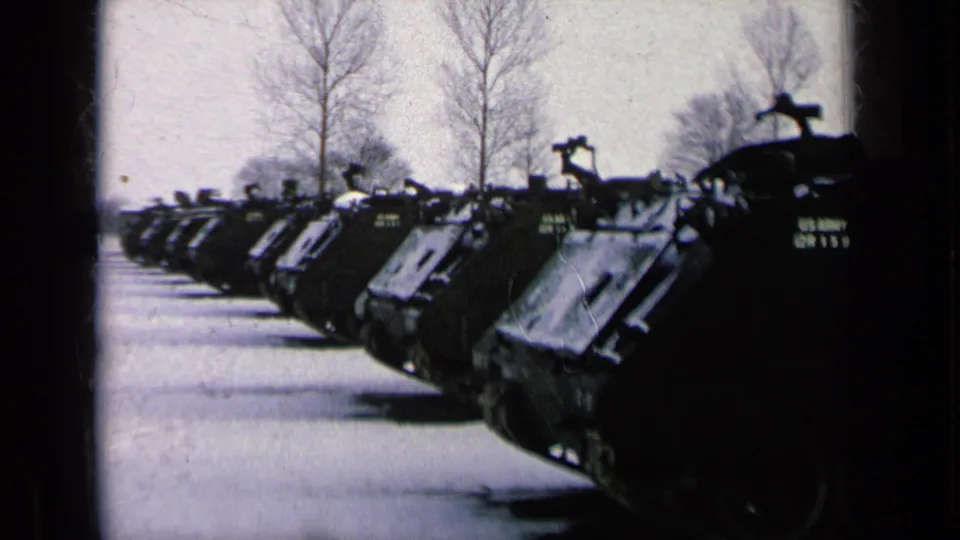 Wide 1963 8mm frame showing a line of U.S. Army armored personnel carriers parked on a Germany military base.