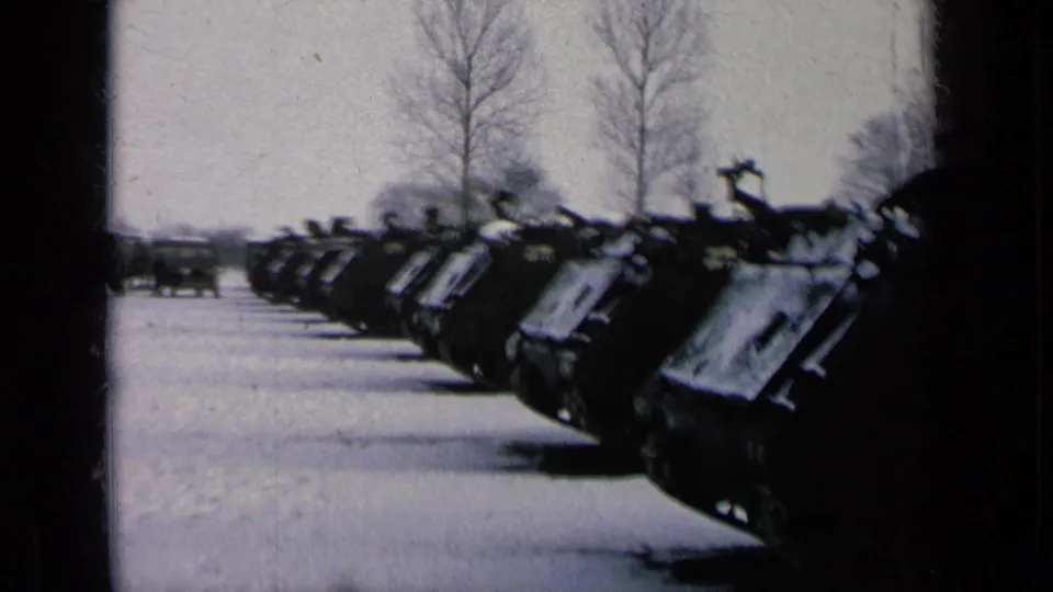 1963 archival home-movie frame showing tanks lined in rows on snow-covered ground, with bare trees beyond the lot.