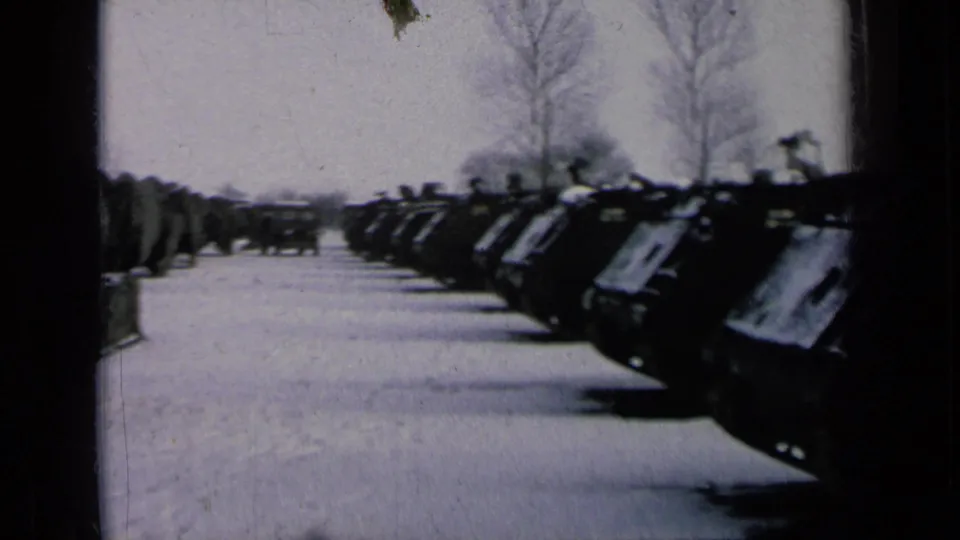 Low-angle 8mm frame of parked tanks receding across a snow-covered lot under bare winter trees.