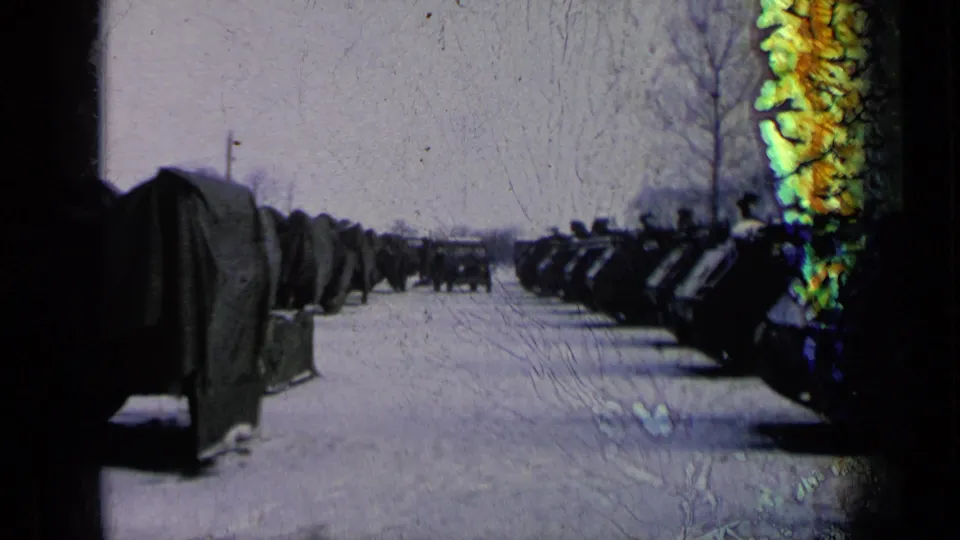 Archival frame showing tanks, possible covered equipment, snow, bare trees, and a visible film artifact over the scene.