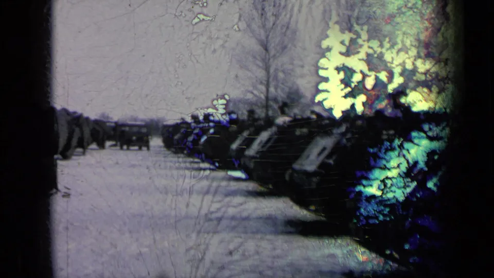 1963 8mm frame of armored vehicles lined beside a snowy base road, with a distant truck and visible light-leak damage.