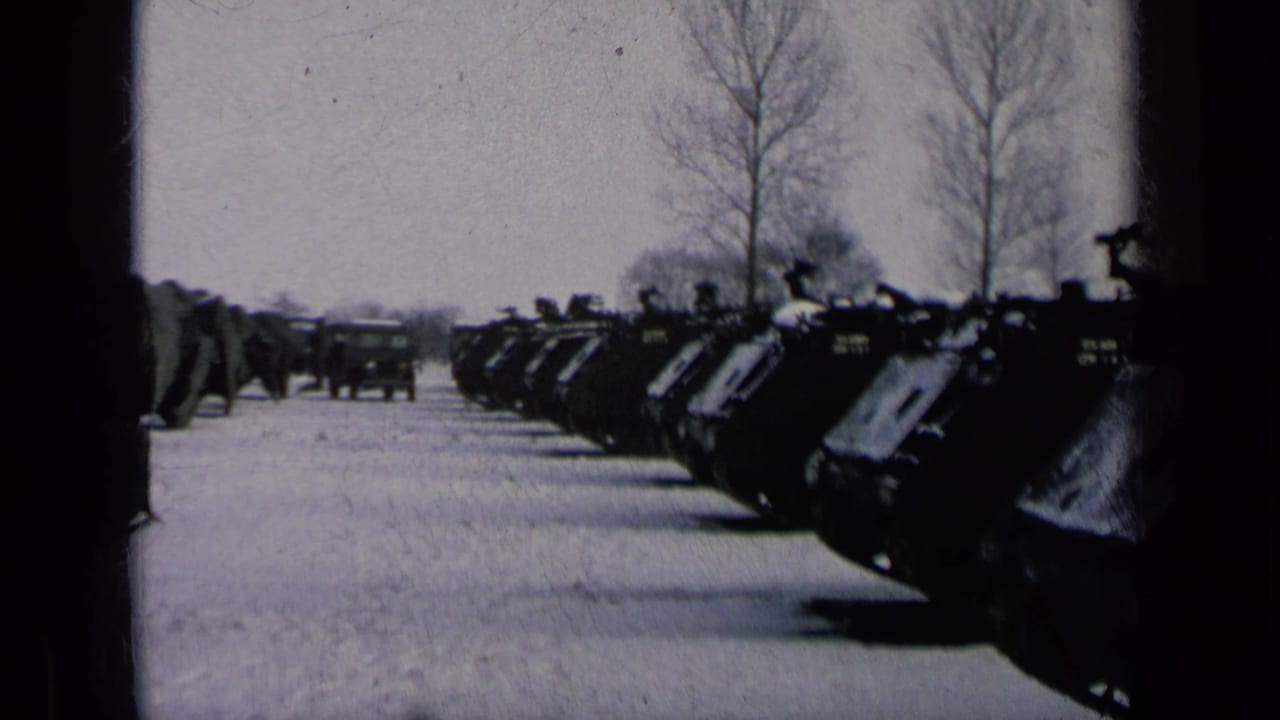 Line of dark military vehicles beside a snowy road, with a truck farther ahead.