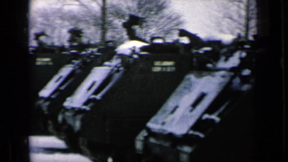 Close 8mm view of snow-dusted armored vehicles, with indistinct personnel silhouettes near the vehicle tops.