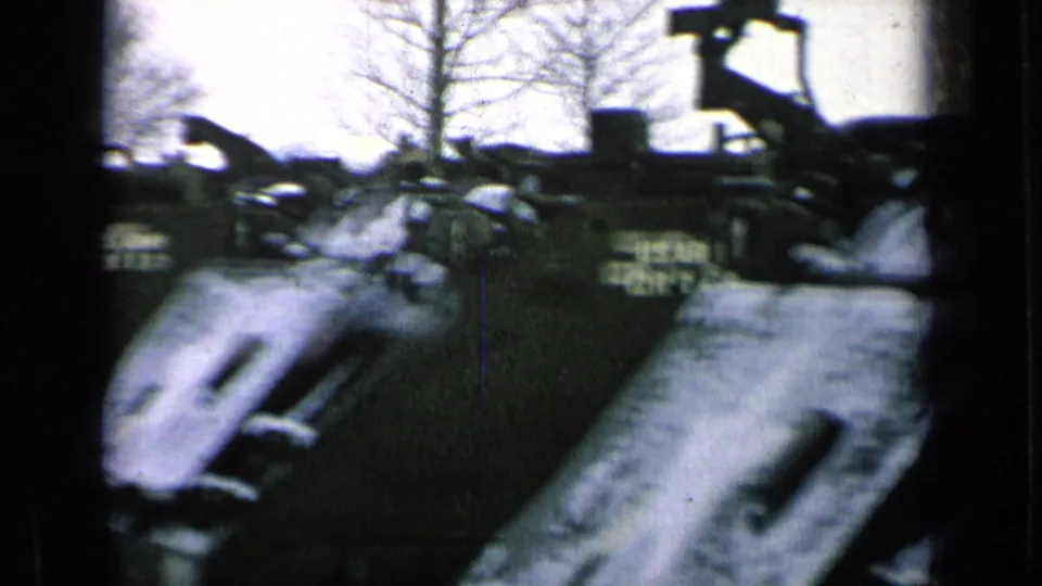 1963 8mm frame of U.S. Army armored vehicles parked in a row on a German military base, with bare trees in the background.