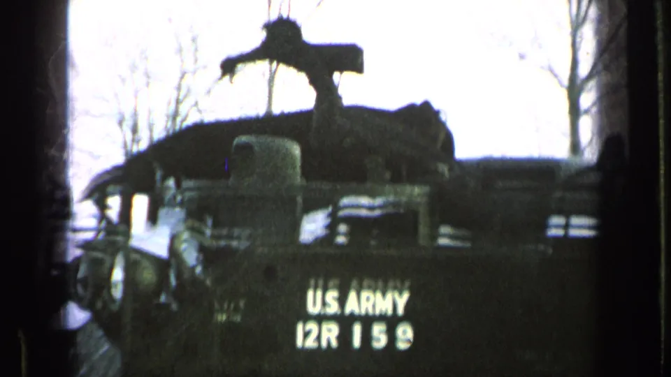 Close 8mm view of the rear of a U.S. Army armored vehicle marked 12R 159, with equipment silhouetted above it.