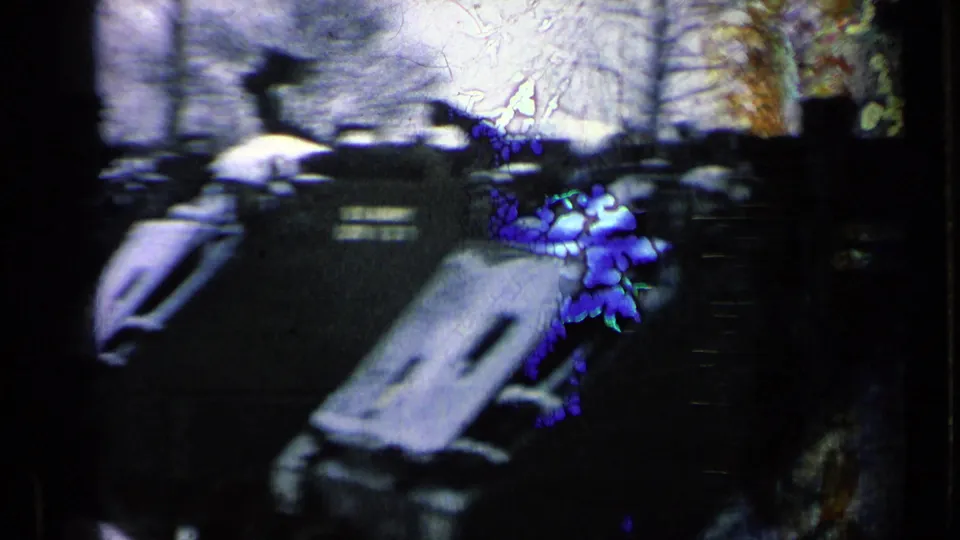Grainy 8mm frame showing several U.S. Army armored vehicles parked close together, with film damage and bare trees visible.