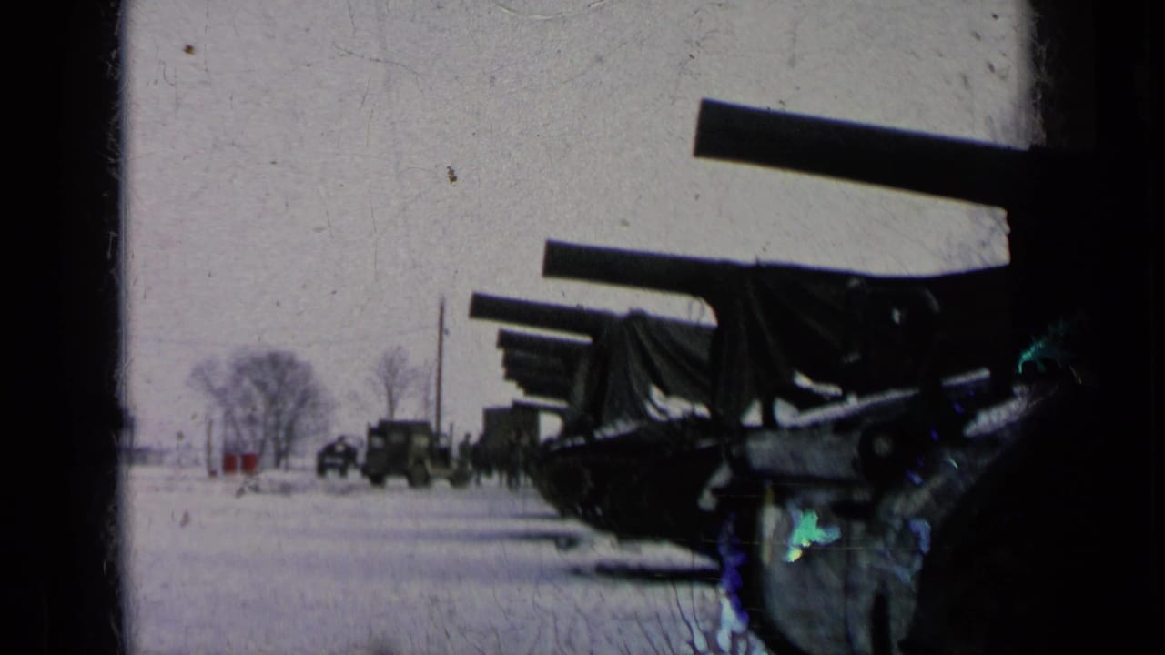 Covered artillery in the foreground with trucks and soldiers farther away.