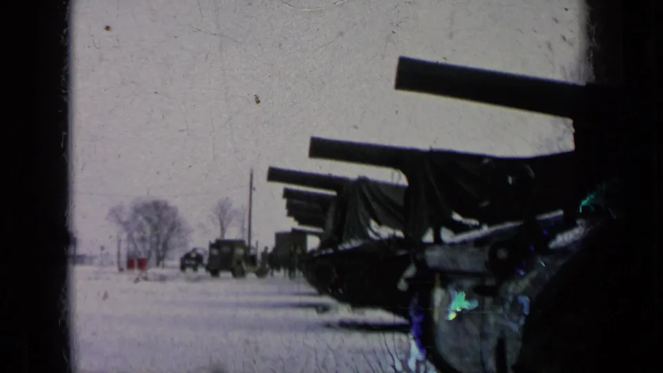 Covered artillery dominates the snowy foreground, with military vehicles and small distant personnel visible beyond it.