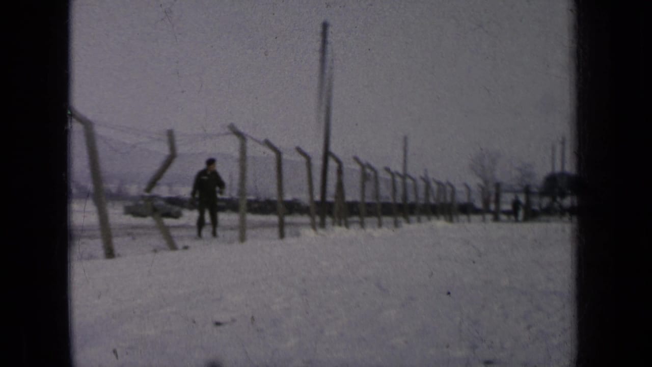 Uniformed man walks in snow beside a barbed-wire fence.