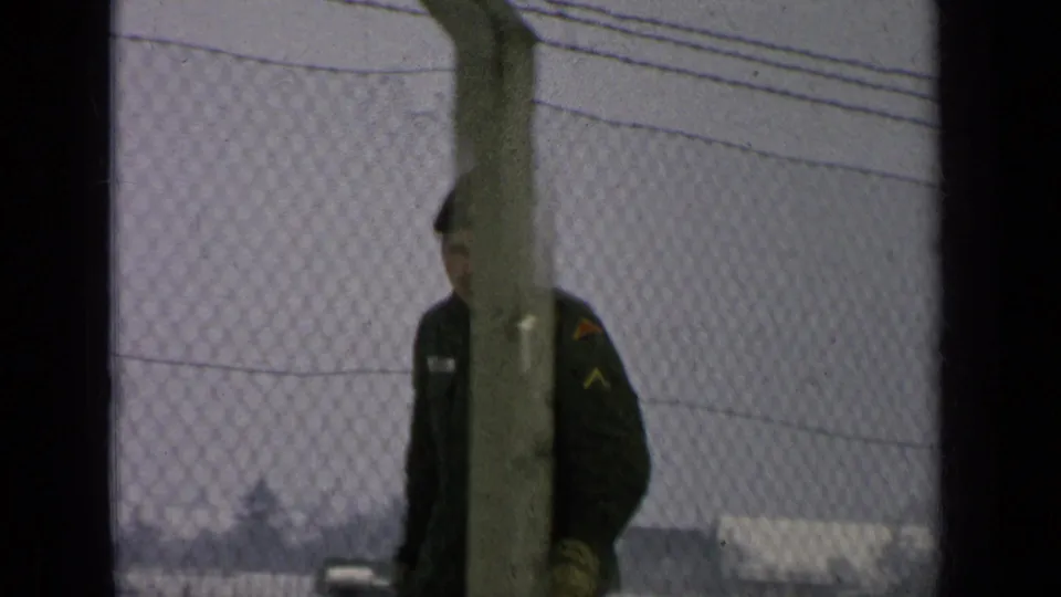 A fence post obscures part of the uniformed man as he passes the chain-link fence in the snowy base setting.