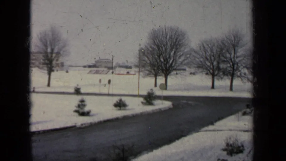 1963 8mm view from a window toward a snowy road on a Germany military-base area, with bare trees and distant buildings.