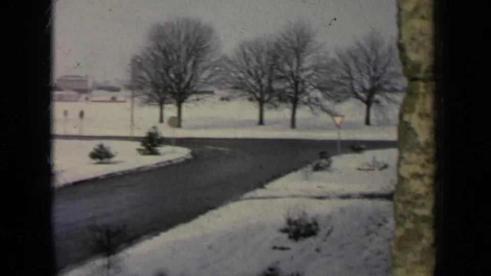 Snowy Germany base-area road in 1963, framed by bare winter trees, small shrubs, and distant low buildings.