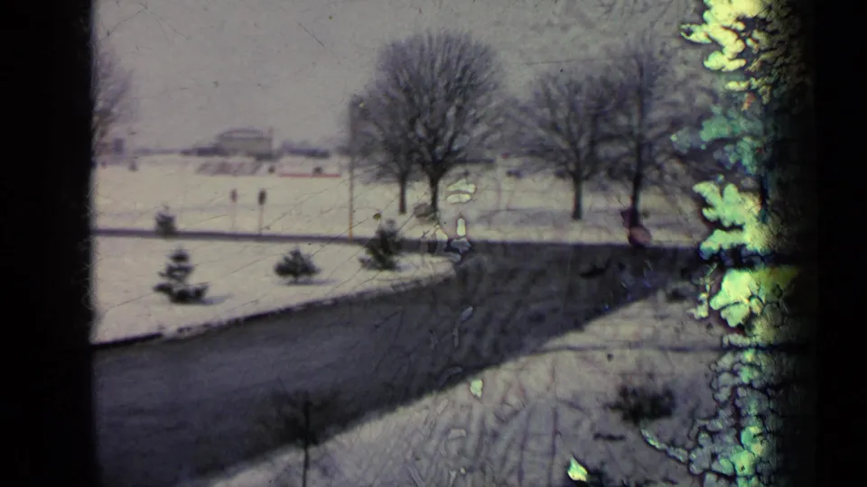 Window-framed 8mm view of a snowy road and winter trees in Germany, with visible film wear and color fading.
