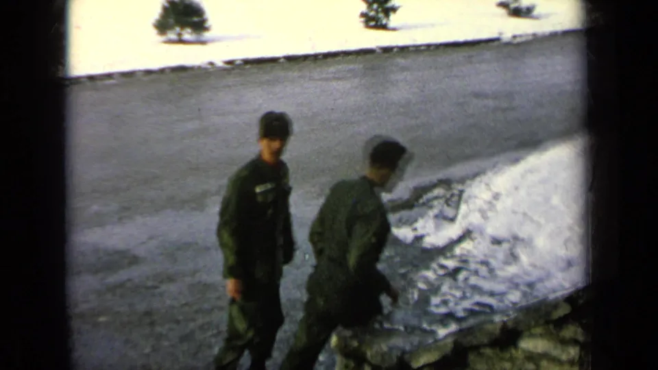 One uniformed man turns toward the camera as another walks down the steps, with snow, road, and winter landscaping visible.