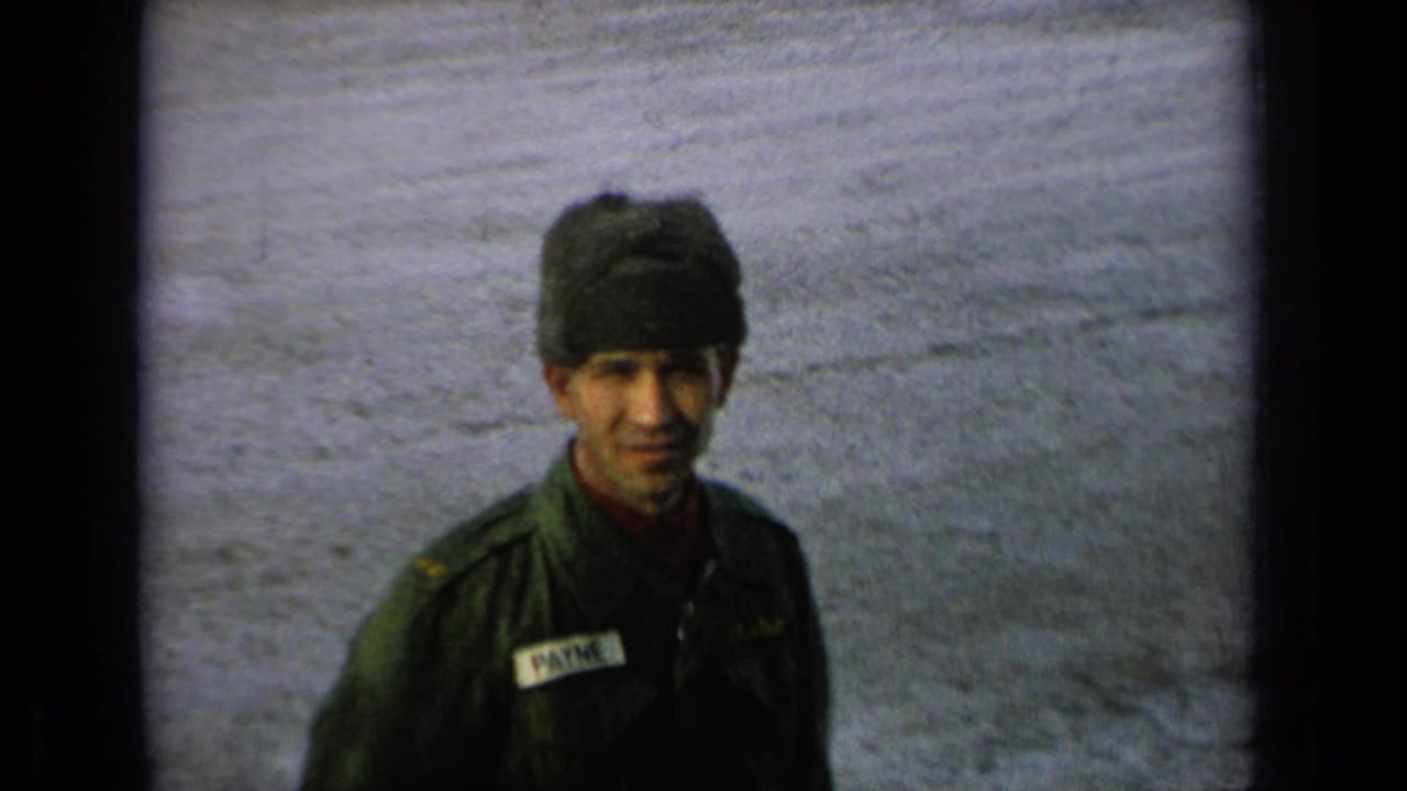 Uniformed man in winter hat standing outdoors or near a pale surface.