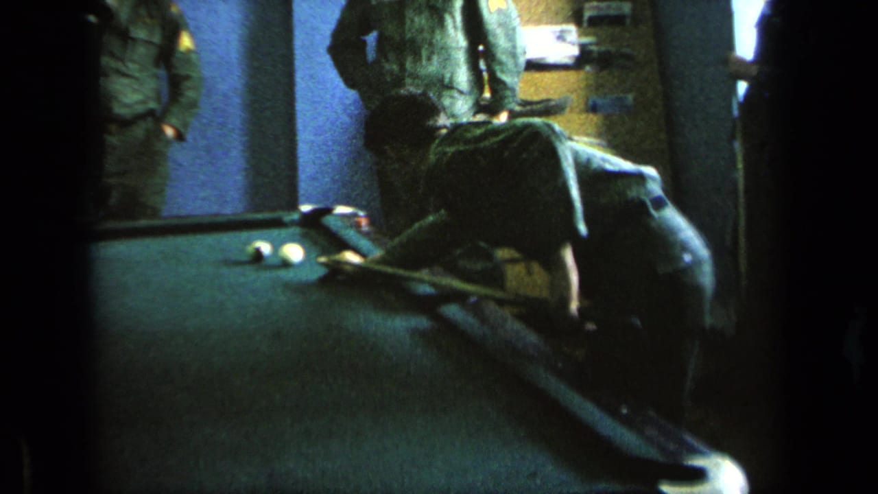 Uniformed men around a pool table as one man bends to take a shot.