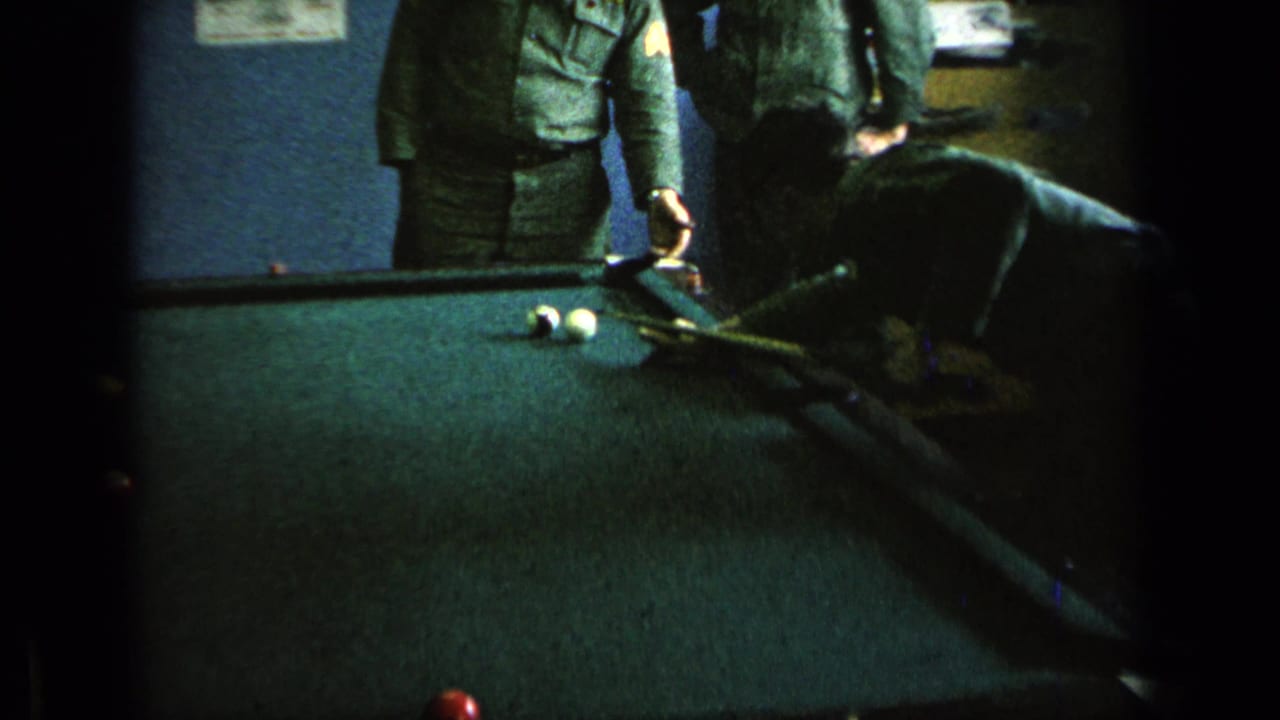 Uniformed men stand around a green pool table in a dim recreation room.