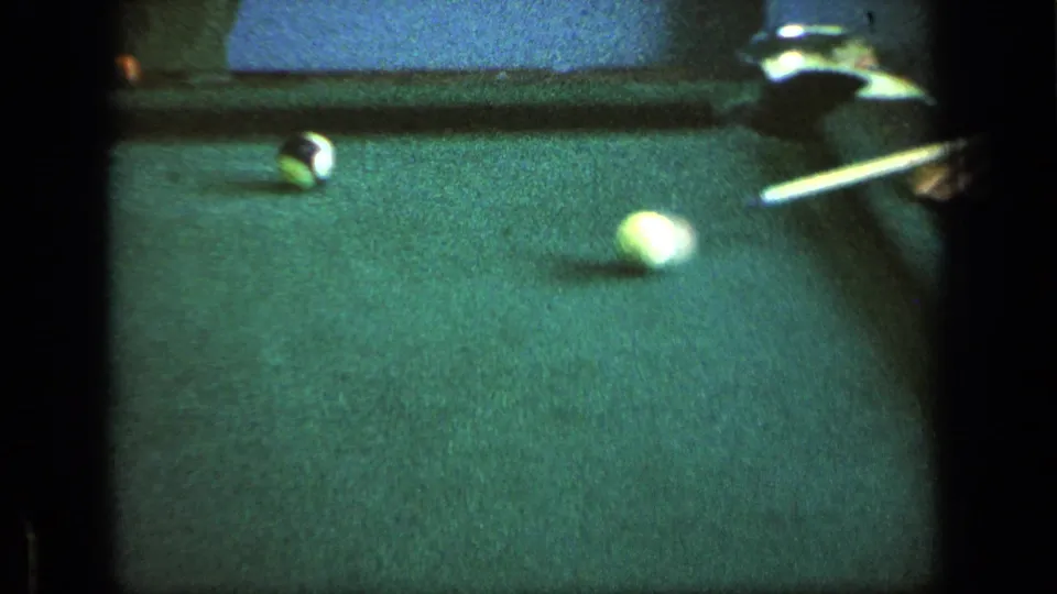 Close 8mm view of billiard balls on green felt, with a cue entering from the right edge of the frame.