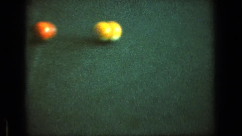 Soft 8mm close-up of red and yellow billiard balls resting on green felt during a pool game.