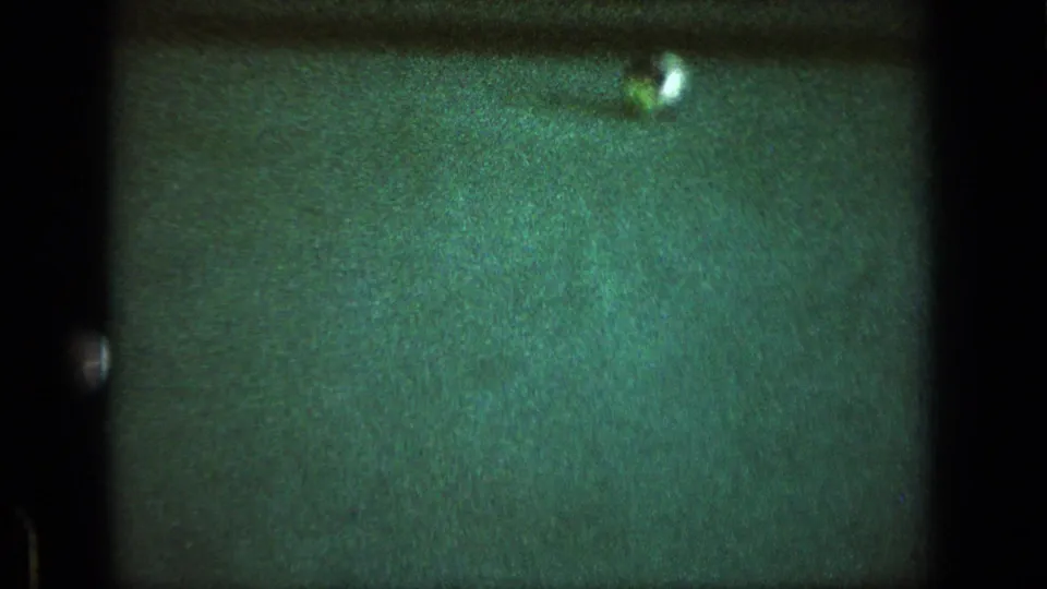 A white billiard ball sits on the green pool table in a softly exposed 8mm frame from the game.