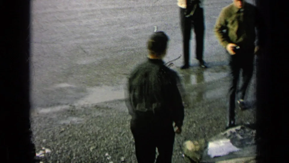 Home-movie frame from a Germany military-base setting with men repositioning on wet pavement, one seen from behind and another partly cropped.
