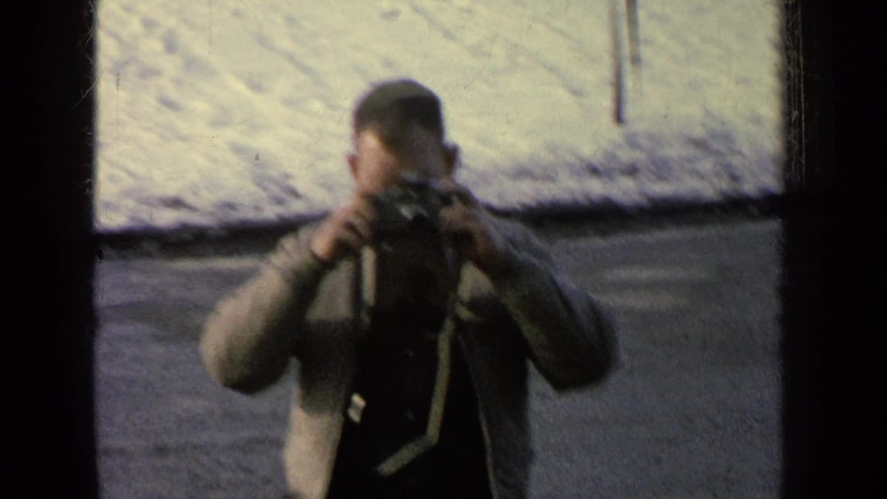 Man holding a camera beside a snowy road, partly obscured by dark film borders.
