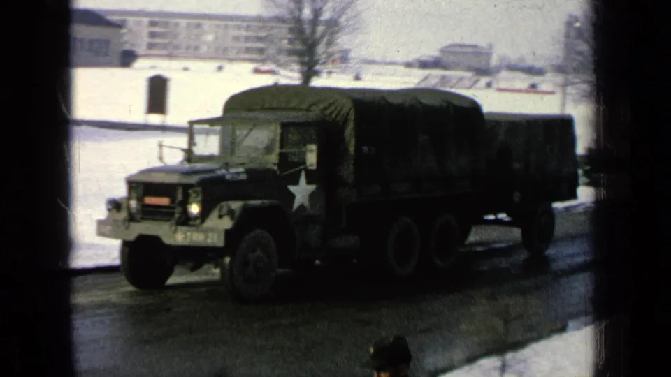 The green cargo truck passes closer to the camera, with a white star marking visible against the snowy base road.