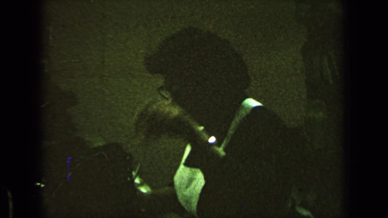 Man in glasses leans over a desk in dim, grainy footage.