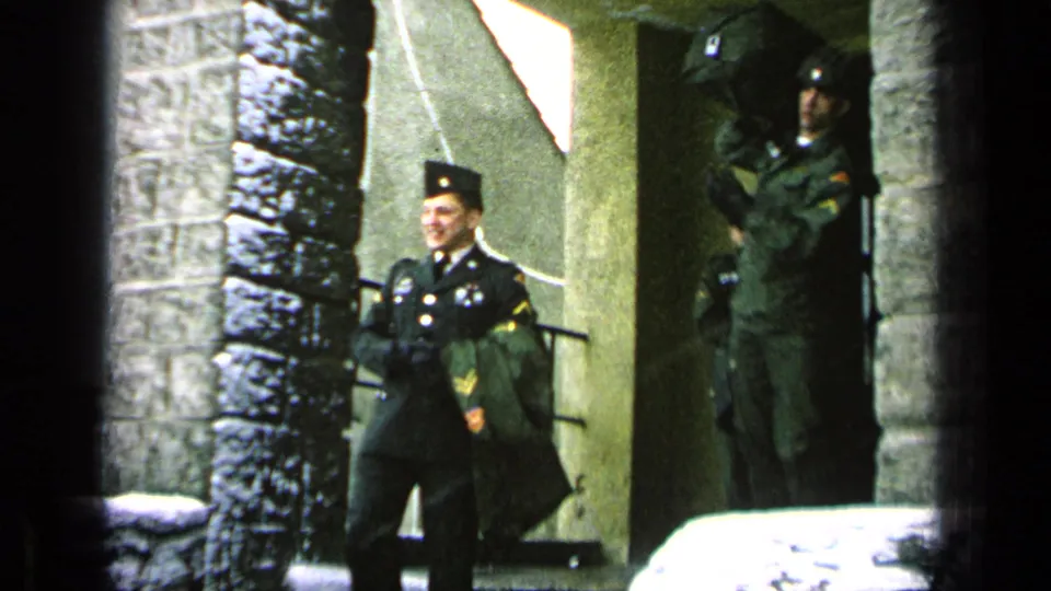 Uniformed soldiers appear outside near a stone archway and entrance, with one figure standing in formal dress.
