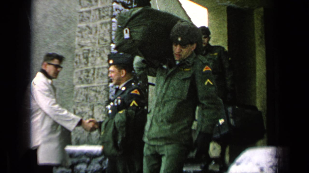Soldier with a large duffel bag stands near a handshake outside a snowy building entrance.