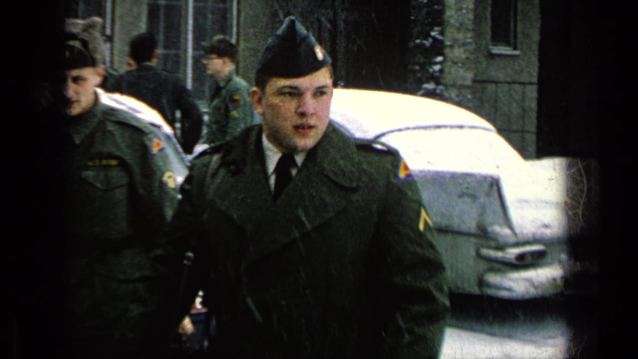 Uniformed soldiers stand near a snow-covered car outside base buildings.