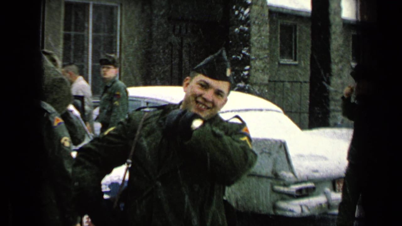 A smiling soldier waves toward the camera beside a snowy car.