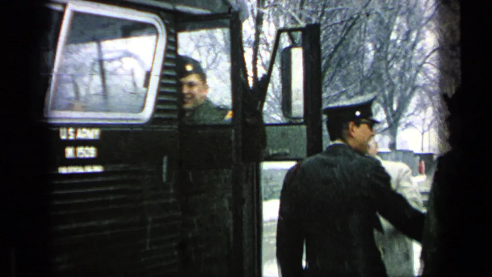 A uniformed soldier looks toward the camera near a U.S. Army bus as others gather by the door.