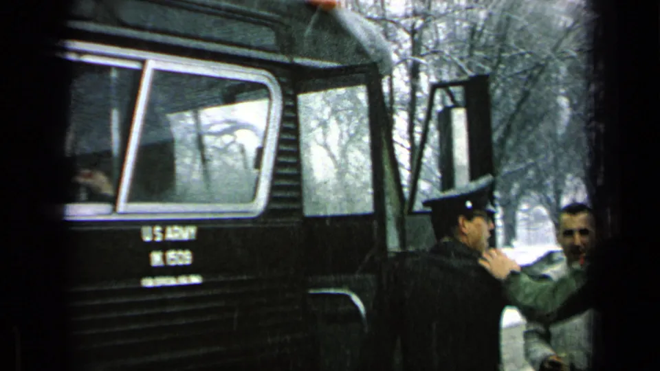Men stand beside the marked U.S. Army bus, with one soldier near the doorway and bare trees in the background.