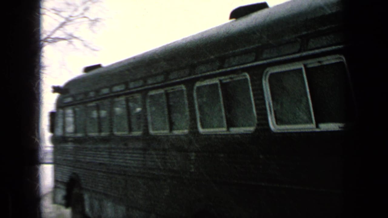 Dark bus seen from the side on a snowy road, partly obscured by the film frame edge.