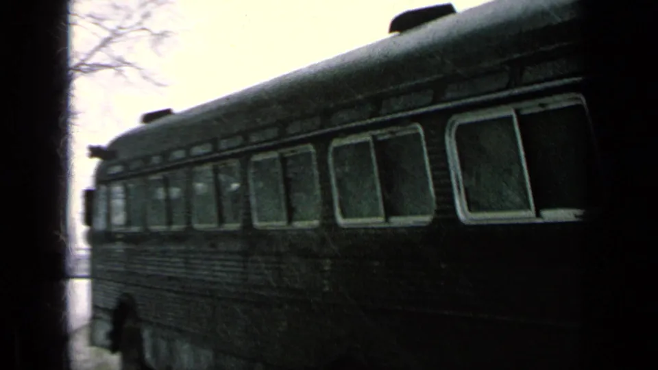 1963 8mm frame of a dark bus passing close to camera on a snow-covered road at a reported Germany military-base setting.