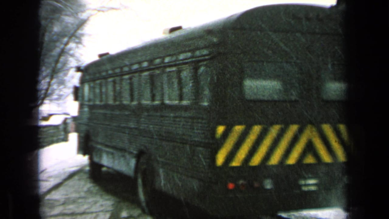 Dark bus departing in snow, with yellow rear hazard stripes and bare trees visible in the reported military-base setting.