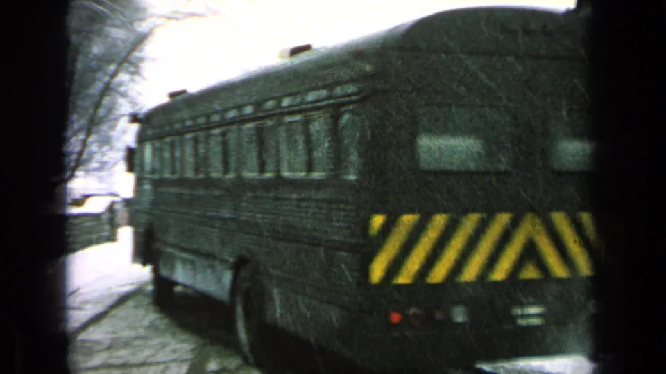 Dark bus departing in snow, with yellow rear hazard stripes and bare trees visible in the reported military-base setting.