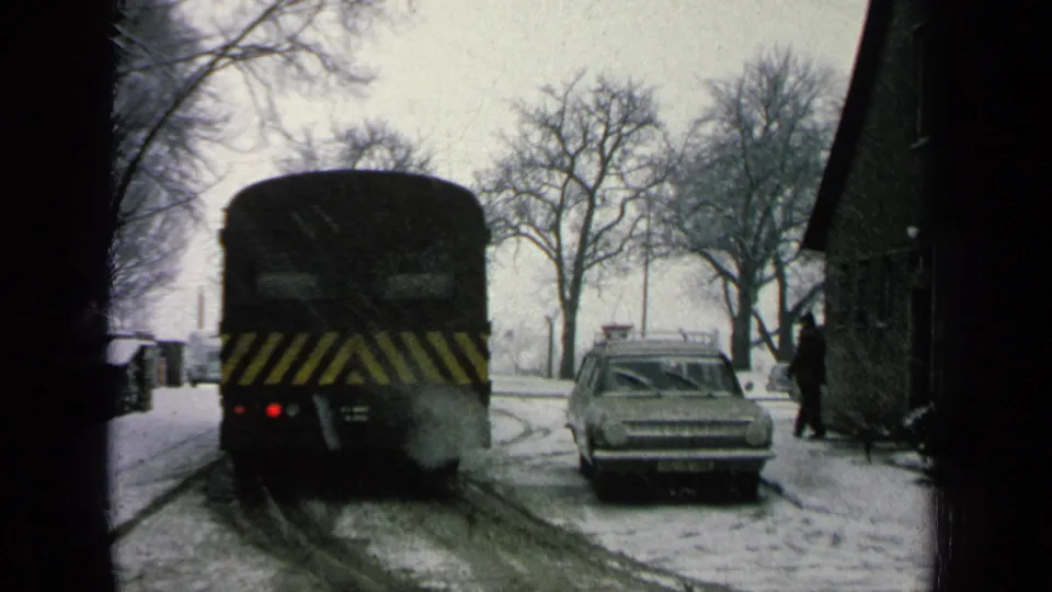 Final frame shows the bus farther away on the snowy road, a parked sedan beside it, and a distant person near the building at right.