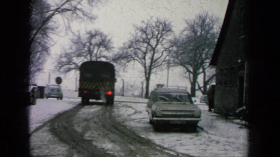 Final frame shows the bus smaller in the distance on the snowy road, with the station wagon, roadside sign, bare trees, and building edge still visible.