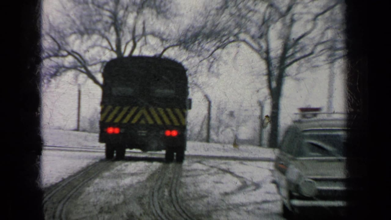 Bus with red taillights follows snowy tire tracks as a station wagon appears at right.