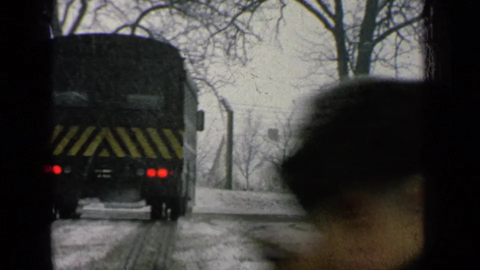 Close 8mm frame of the bus rear on a snow-covered base road, with taillights and yellow striping visible.