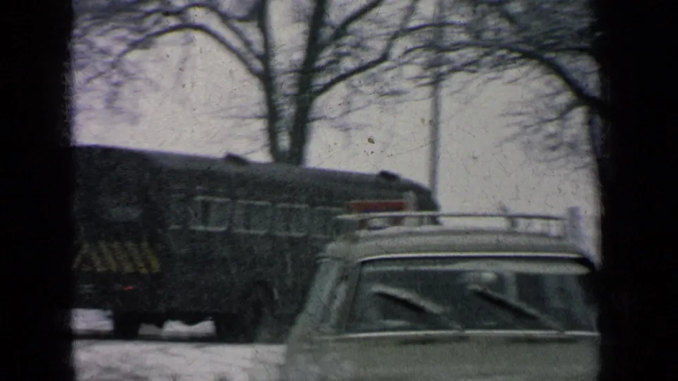 The dark bus moves past a station wagon on a snowy road in 1963 Germany military base home-movie footage.
