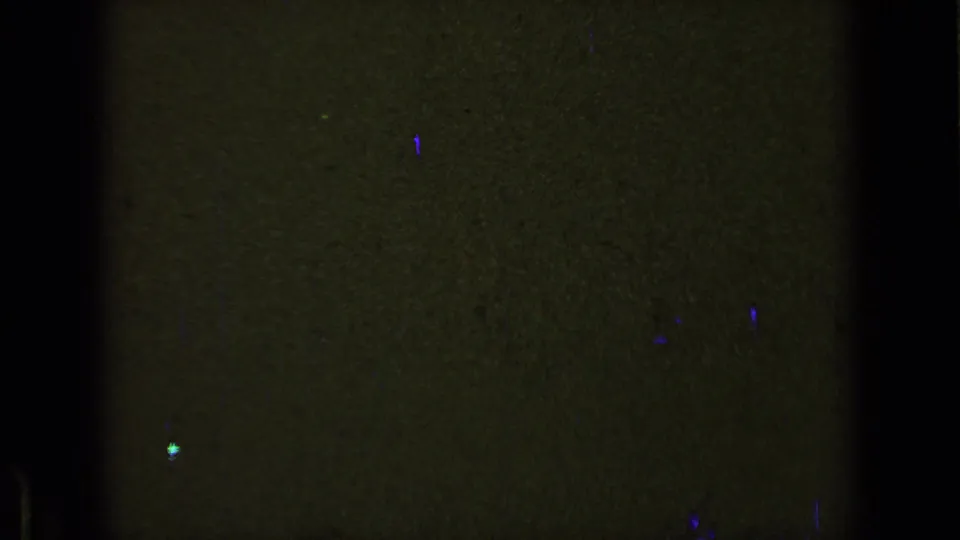 Dark 8mm frame from the 1963 reel showing olive-green exposure, black gate edges, grain, scratches, and scattered blue-purple marks.