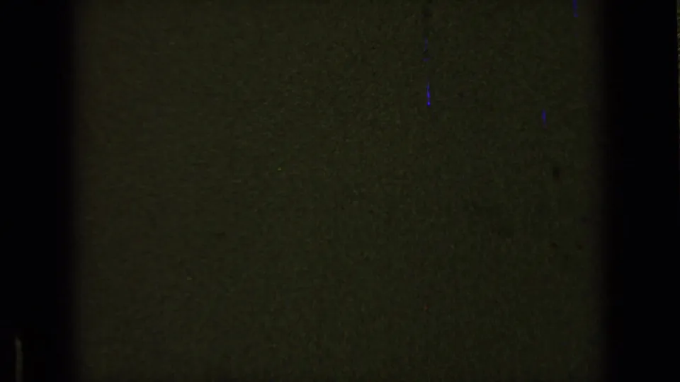 Dark abstract 8mm frame with green exposure, heavy black borders, fine grain, faint scratches, and blue-purple flecks.
