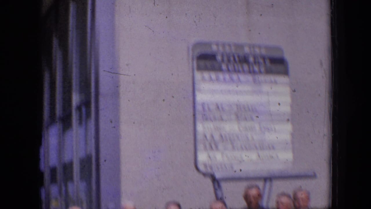 A soft, handheld 1963 London frame shows an airline sign on a building exterior with heads partly visible at the lower edge.
