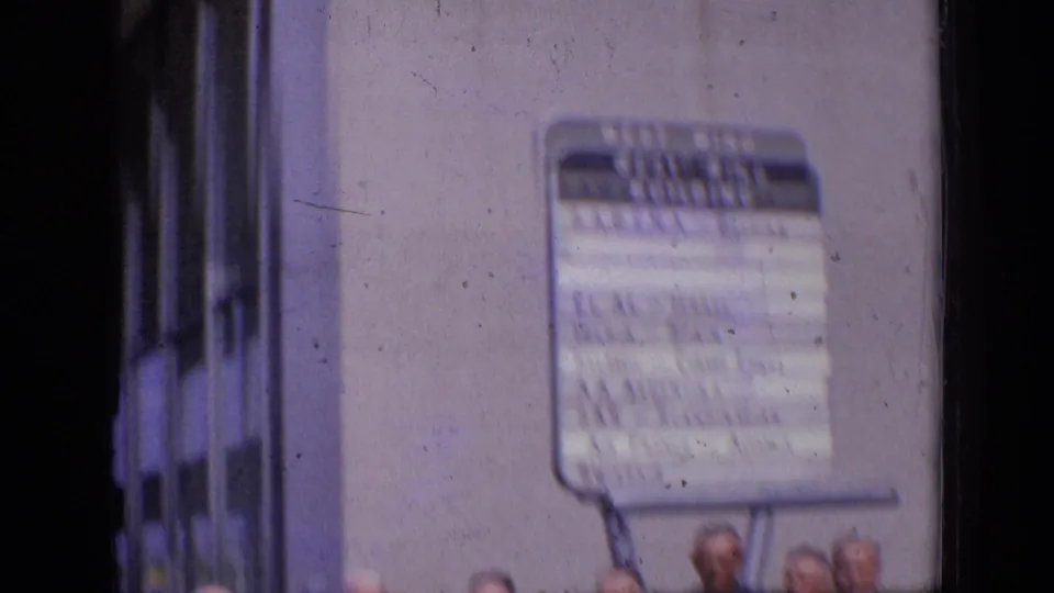 A soft, handheld 1963 London frame shows an airline sign on a building exterior with heads partly visible at the lower edge.