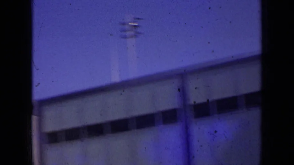 The camera passes across a modern London building facade, showing soft focus, windows, and dark film borders.