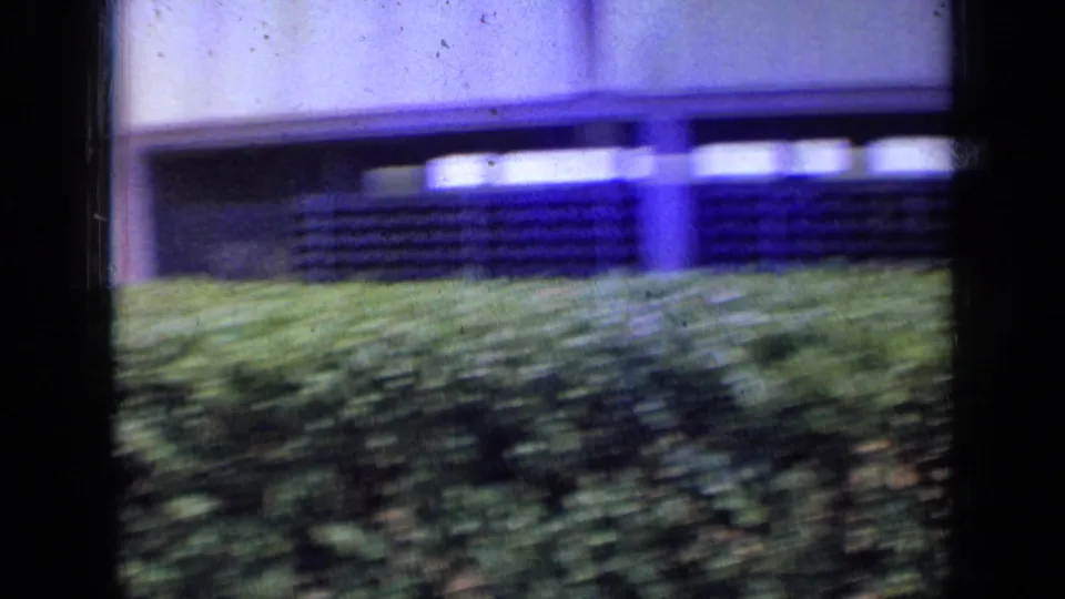 A 1963 London exterior cutaway shows the building edge, rows of windows, and green bushes in soft 8mm color.